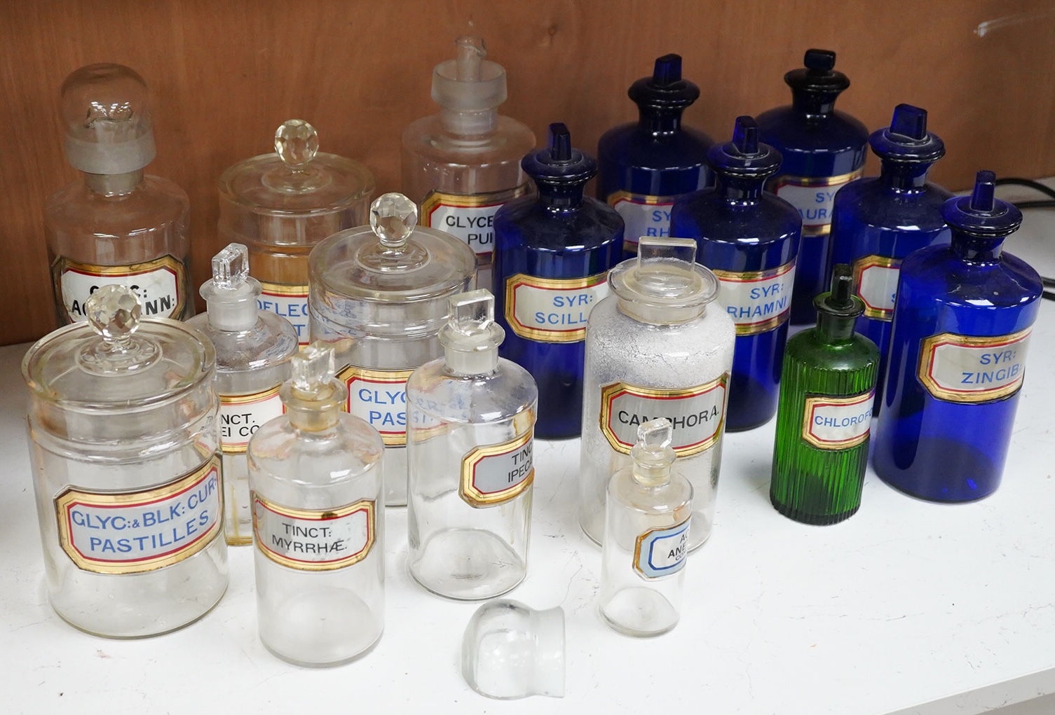 Seventeen 19th/early 20th century glass apothecary jars with gilt rimmed labels; six blue glass, ten clear glass and a green glass example, labels including; Syr: Zingib:, Chloroform, Syr: Rhei:, Camphora, etc. tallest 2